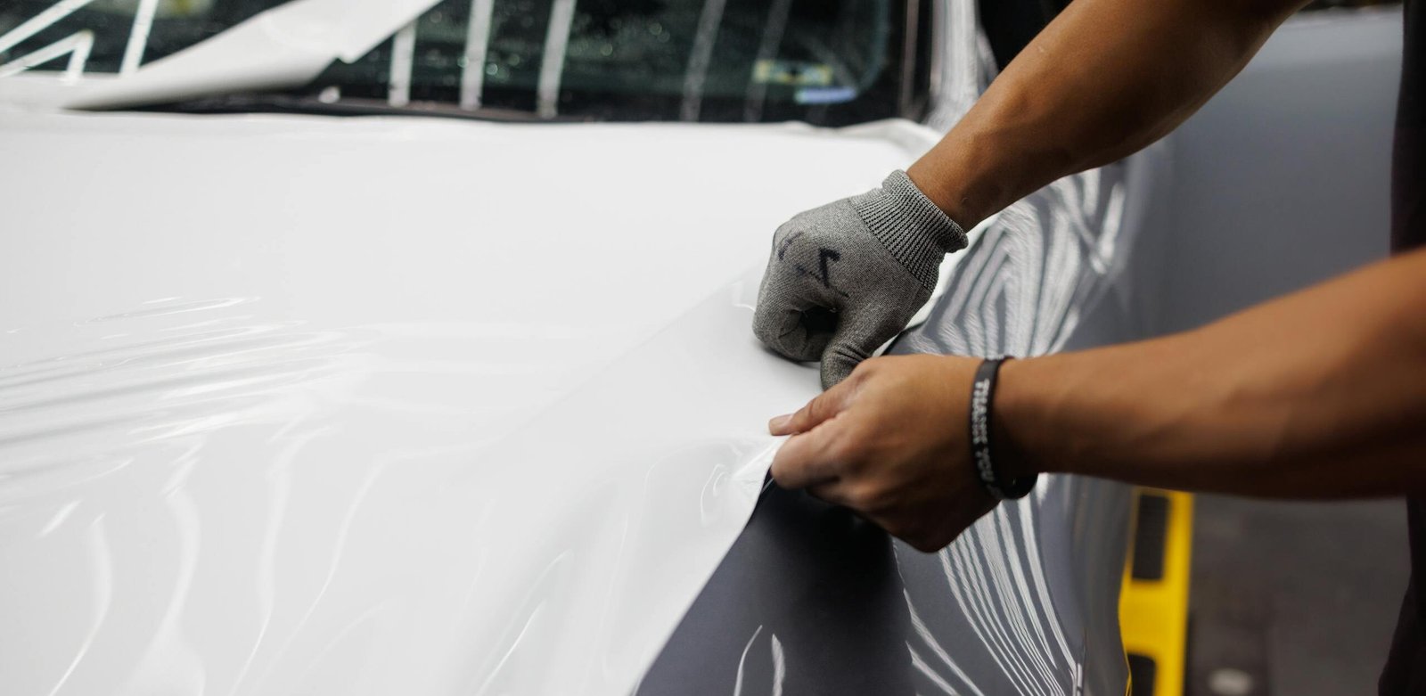Close-up of hands applying vinyl wrap to a car hood, showcasing customization.